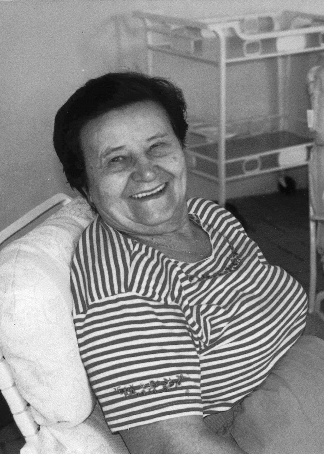 A smiling woman with short dark hair, wearing a striped shirt, sitting on a chair on a patio